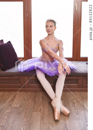 portrait of a beautiful little ballerina in a performance purple dress sitting by the window and dreaming to become professional ballet dancer 89132622