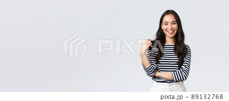 Lifestyle, people emotions and casual concept. Charming smiling korean girl in striped shirt, touching hair strand and grinning happily camera, talking to friend, white background 89132768