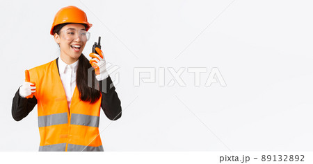 Satisfied happy smiling asian female engineer, industrial technician in safety helmet and uniform showing thumbs-up while praising great work using walkie-talkie, give permission to work Satisfied happy smiling asian female engineer, industrial technician in safety helmet and uniform showing thumbs-up while praising great work using walkie-talkie, give permission to work 89132892