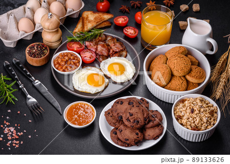 A delicious nutritious healthy breakfast with fried eggs, bacon, beans, a glass of juice, oat cookies, milk and jam A delicious nutritious healthy breakfast with fried eggs, bacon, beans, a glass of juice, oat cookies, milk and jam 89133626