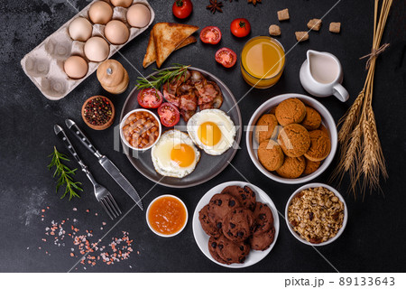 A delicious nutritious healthy breakfast with fried eggs, bacon, beans, a glass of juice, oat cookies, milk and jam A delicious nutritious healthy breakfast with fried eggs, bacon, beans, a glass of juice, oat cookies, milk and jam 89133643