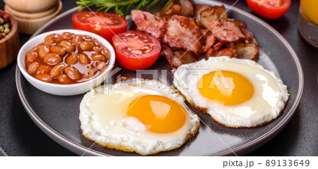 A delicious nutritious healthy breakfast with fried eggs, bacon, beans, a glass of juice, oat cookies, milk and jam 89133649
