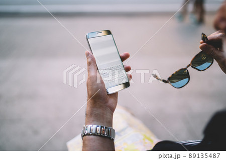 Unrecognizable man reading text publication during text chatting on cellphone 89135487