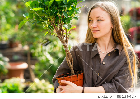 Girl florist with a plant in a pot in her hand looks to the side 89136427