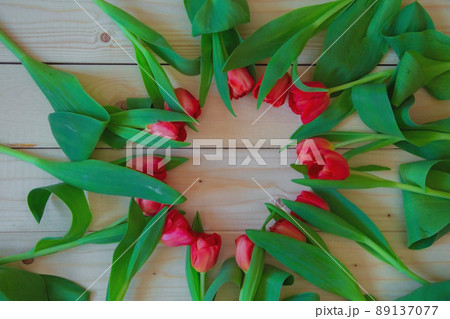 Pink tulips with green leaves lie in a circle with a free place in the center on a wooden background. High quality photo 89137077