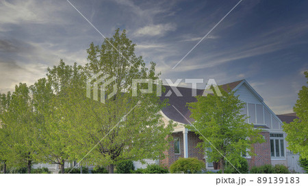 Panorama Whispy white clouds Corner house with bricks siding, flowers and trees on the lawn a Panorama Whispy white clouds Corner house with bricks siding, flowers and trees on the lawn a 89139183