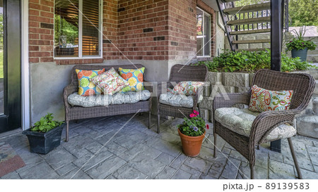 Panorama Woven couch and armchairs on an outdoor patio under the deck of a house with bricks Panorama Woven couch and armchairs on an outdoor patio under the deck of a house with bricks 89139583
