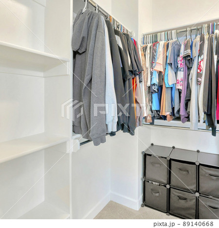 Square Small walk-in closet with hanging sweaters, shirts and blouse on the metal rods 89140668