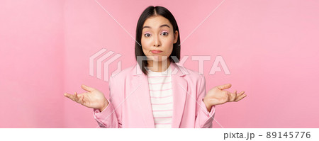 Portrait of confused asian businesswoman shrugging shoulders, looking clueless and puzzled, dont know, cant say, standing over pink background in office suit Portrait of confused asian businesswoman shrugging shoulders, looking clueless and puzzled, dont know, cant say, standing over pink background in office suit 89145776