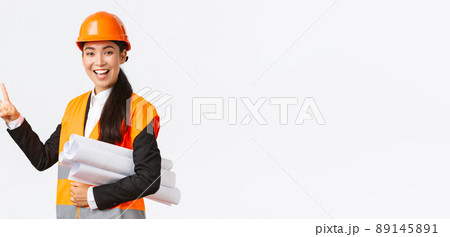 Smiling confident asian female engineer, construction manager in safety helmet, carry blueprints, showing two fingers, ensure building finished in time, standing white background upbeat Smiling confident asian female engineer, construction manager in safety helmet, carry blueprints, showing two fingers, ensure building finished in time, standing white background upbeat 89145891