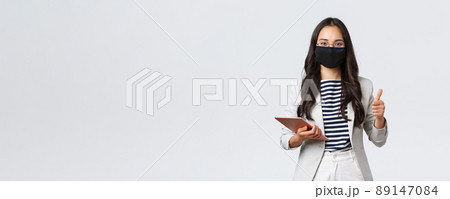 Business, finance and employment, covid-19 preventing virus and social distancing concept. Smiling real estate broker wearing protective mask during meeting, pointing camera, hold digital tablet Business, finance and employment, covid-19 preventing virus and social distancing concept. Smiling real estate broker wearing protective mask during meeting, pointing camera, hold digital tablet 89147084