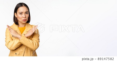 Stop gesture. Serious asian woman making arm cross, prohibit smth, rejecting, dislike and disapprove action, standing over white background Stop gesture. Serious asian woman making arm cross, prohibit smth, rejecting, dislike and disapprove action, standing over white background 89147582