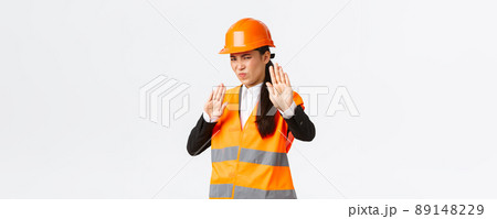 Displeased and reluctant asian female architect in safety helmet grimacing from aversion, showing stop gesture, refuse or rejecting awful disgusting plan, standing disappointed white background Displeased and reluctant asian female architect in safety helmet grimacing from aversion, showing stop gesture, refuse or rejecting awful disgusting plan, standing disappointed white background 89148229