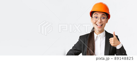 Close-up of professional pleased asian female chief engineer, architect in business suit and safety helmet showing thumbs-up in approval, give permission, recommend construction company Close-up of professional pleased asian female chief engineer, architect in business suit and safety helmet showing thumbs-up in approval, give permission, recommend construction company 89148825
