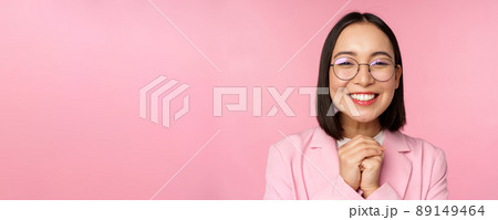Close up portrait of smiling happy businesswoman in glasses, clench hands together thankful, excited of smth, begging or say please, standing over pink background 89149464