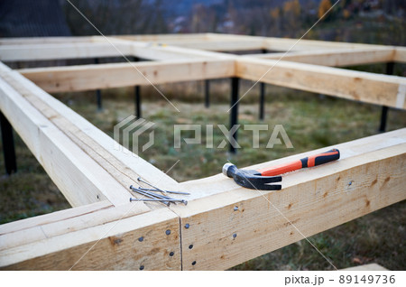 Hammer and nails laying on wooden pile foundation for future frame house. Constuction site and work instrument concept. Hammer and nails laying on wooden pile foundation for future frame house. Constuction site and work instrument concept. 89149736
