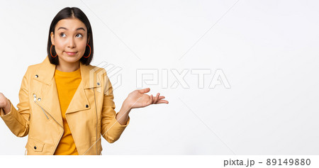 Image of korean girl shrugs shoulders and looks confused, dont know, cant tell, standing over puzzled over white background 89149880