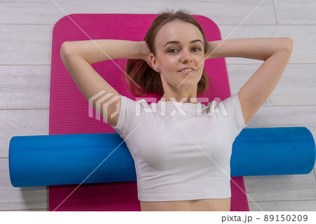 The girl lies fitness mfr roller the on red mat mfr sportswear, from fit cheerful for exercise from young workout, pilates sporty. Gymnastics copy space, practicing pose 89150209
