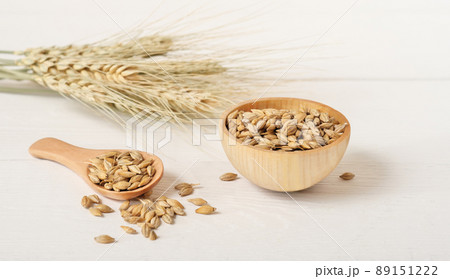 barley grain in a bowl and in wooden spoon next to barley spikes on a table. cereal ears. beer ingredient barley grain in a bowl and in wooden spoon next to barley spikes on a table. cereal ears. beer ingredient 89151222
