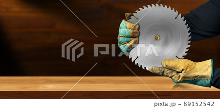 Gloved Hands Holding a Metal Circular Saw Blade on a Wooden Workbench 89152542