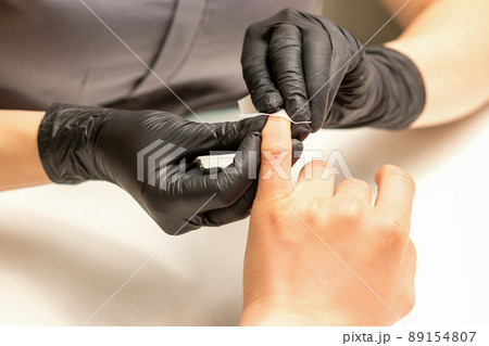 The manicurist finishes the procedure for red nail polishing and cleaning with a cotton napkin, pad, swab in a beauty salon, close up 89154807