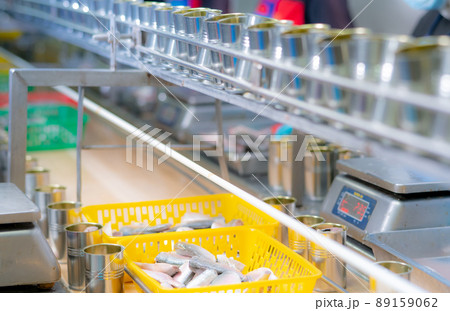 Canned fish factory. Food industry. Sardines in yellow plastic basket waiting for worker to fill in tinned cans. Food processing production line. Food manufacturing industry. Many can on conveyor belt Canned fish factory. Food industry. Sardines in yellow plastic basket waiting for worker to fill in tinned cans. Food processing production line. Food manufacturing industry. Many can on conveyor belt 89159062