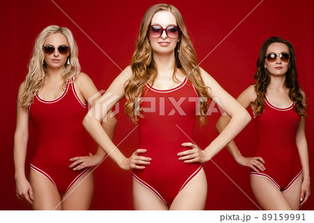 Three women in red swimsuits on a red background Three women in red swimsuits on a red background 89159991