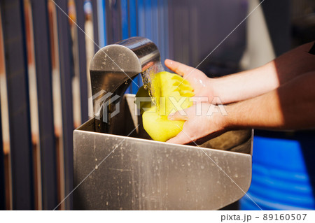 Men's hands wet a yellow car wash sponge at the self-service car wash. 89160507