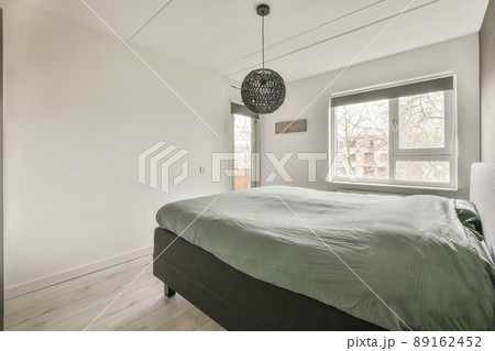 A small bedroom in white tones with a large bed and a window overlooking the street A small bedroom in white tones with a large bed and a window overlooking the street 89162452