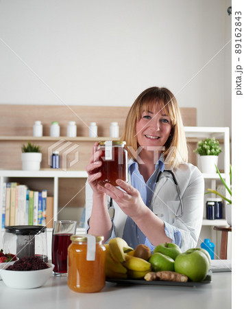 Female nutritionist holding honey in office studio Female nutritionist holding honey in office studio 89162843