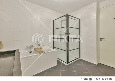 Spacious bathroom with white tiles, bathtub and glass shower stall 89163446