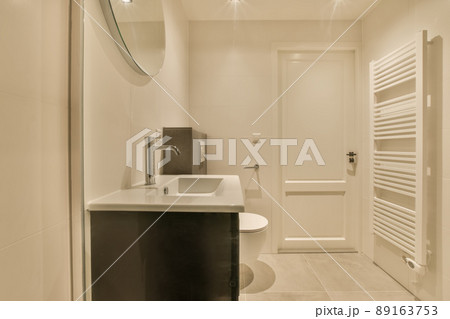 The interior of the bathroom with a toilet and a ceramic sink under a round mirror 89163753