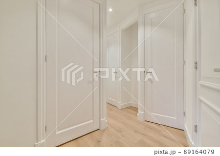 Interior of long narrow hallway with closed door, wooden floor and white walls in apartment designed in minimal style. 89164079