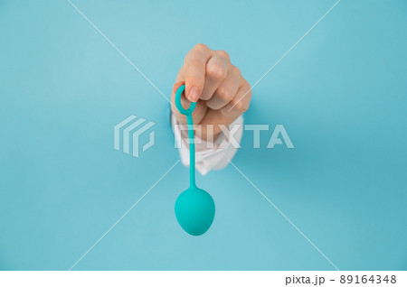A woman's hand sticks out of a hole in a blue background and holds a vaginal egg. A woman's hand sticks out of a hole in a blue background and holds a vaginal egg. 89164348