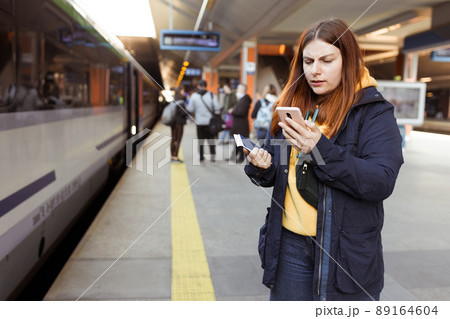 Young redhhead woman waiting on station platform with backpack on background electric train using smart phone. Railroad transport concept, Traveler Young redhhead woman waiting on station platform with backpack on background electric train using smart phone. Railroad transport concept, Traveler 89164604