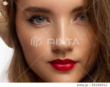 Close up portrait of a face with beautiful skin and evening makeup, eyeliner and long eyelashes, puffy red lips and white flowers. Fashion photography. Cosmetology and spa. Freshness of spring 89166912