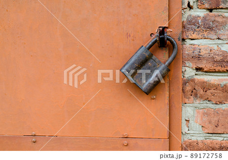 Old padlock on metal door. Red brick wall 89172758