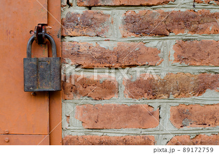 Old padlock on metal door. Red brick wall Old padlock on metal door. Red brick wall 89172759