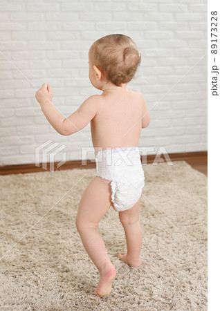 a small child in a disposable diaper against a white wall - view from the back a small child in a disposable diaper against a white wall - view from the back 89173228