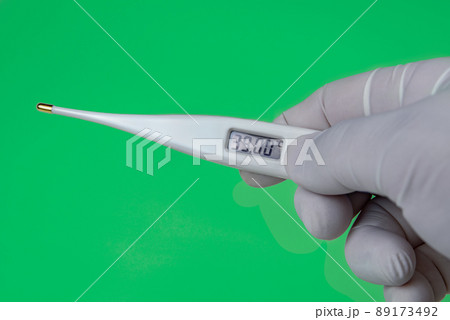 Hand with a Thermometer on Green background. The thermometer shows a temperature of 39 Celsius. Coronavirus 2019-nCoV. Corona virus outbreaking. 89173492