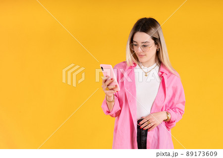 Young woman standing using her cell phone on yellow background 89173609