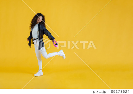 Young woman walking while lifting one foot holding wireless headphones in studio shot 89173624