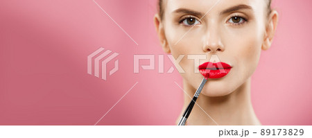 Beauty Concept - Woman applying red lipstick with pink studio background. Beautiful girl makes makeup. 89173829