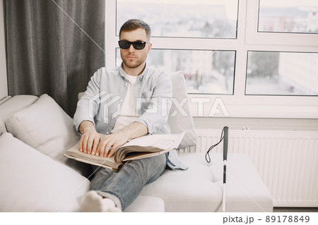 Blind man reading braille book on the couch. disabled people concept. 89178849