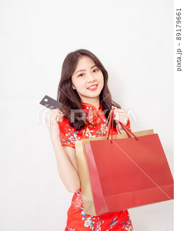 Portrait of a young asian woman wearing traditional cheongsam qipao dress holding shopping bags and showing credit card isolated on wihte background. 89179661