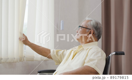 Old asian man sits in a wheelchair and looks out the window Old asian man sits in a wheelchair and looks out the window 89179815