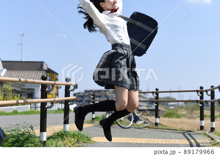 青空の下でジャンプをする笑顔の女子学生 89179966