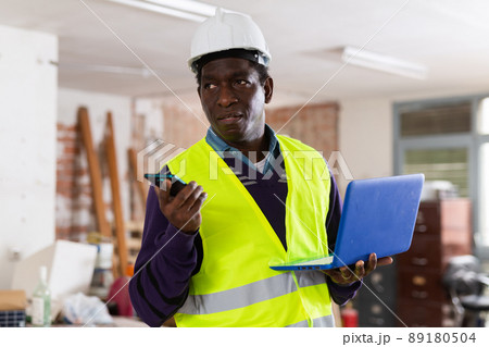Man construction worker with laptop talking ob phone inside apartment Man construction worker with laptop talking ob phone inside apartment 89180504