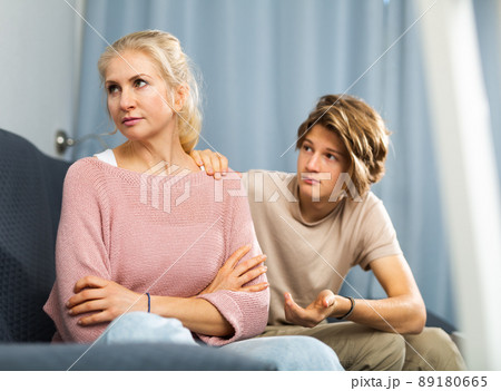 Upset woman sitting at home while teenage son calming her Upset woman sitting at home while teenage son calming her 89180665