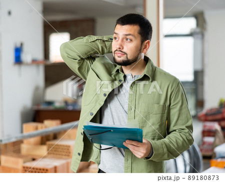Focused man standing at indoors building site, reading document Focused man standing at indoors building site, reading document 89180873